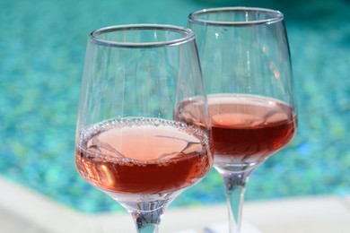 Photo of Glasses of tasty rose wine near swimming pool, closeup