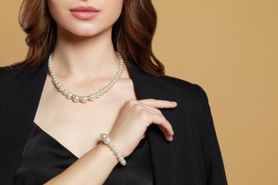 Photo of Young woman wearing elegant pearl jewelry on brown background, closeup