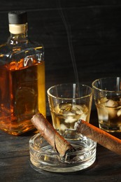 Photo of Cigars, ashtray and whiskey with ice cubes on black wooden table