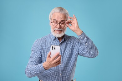 Photo of Portrait of stylish grandpa with glasses using smartphone on light blue background