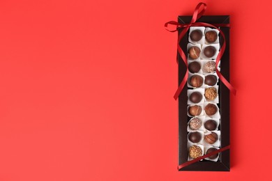 Photo of Box with delicious chocolate candies on red table, top view. Space for text