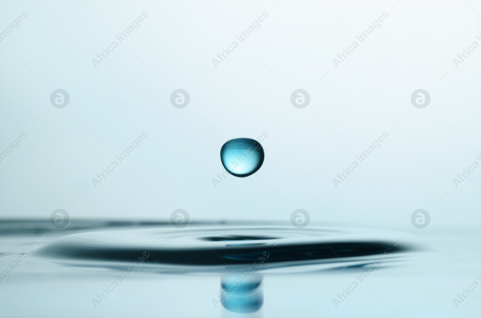 Photo of Drop falling into clear water on light background, closeup