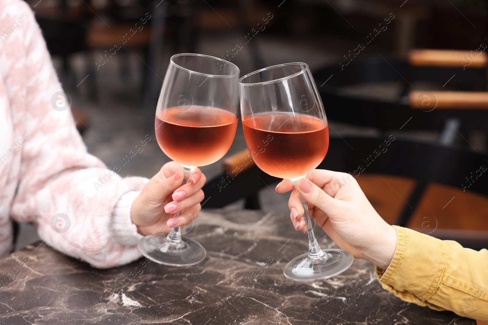 Photo of Women clinking glasses with rose wine at dark marble table in outdoor cafe, closeup