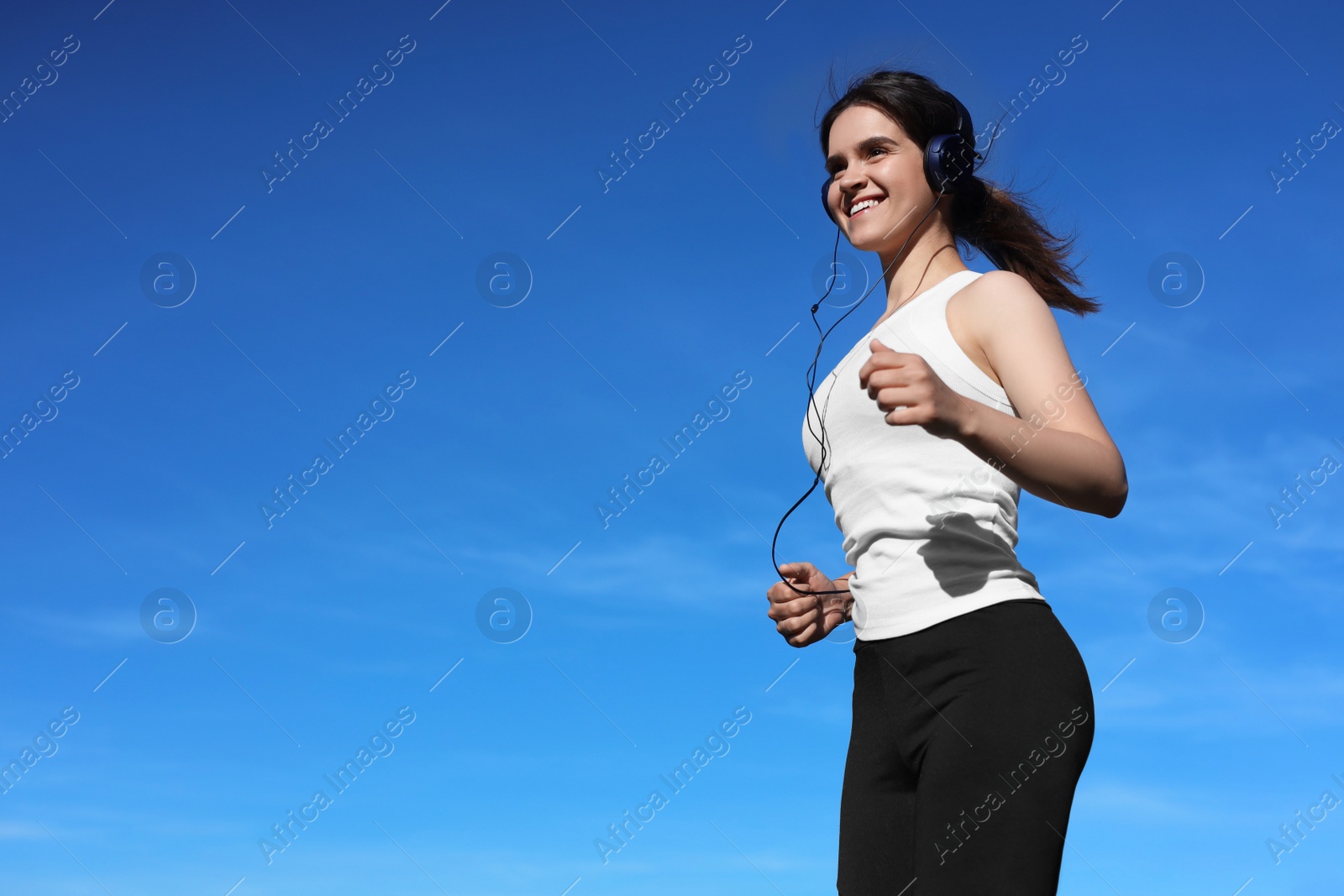 Photo of Young woman listening to music while running outdoors in morning, low angle view. Space for text