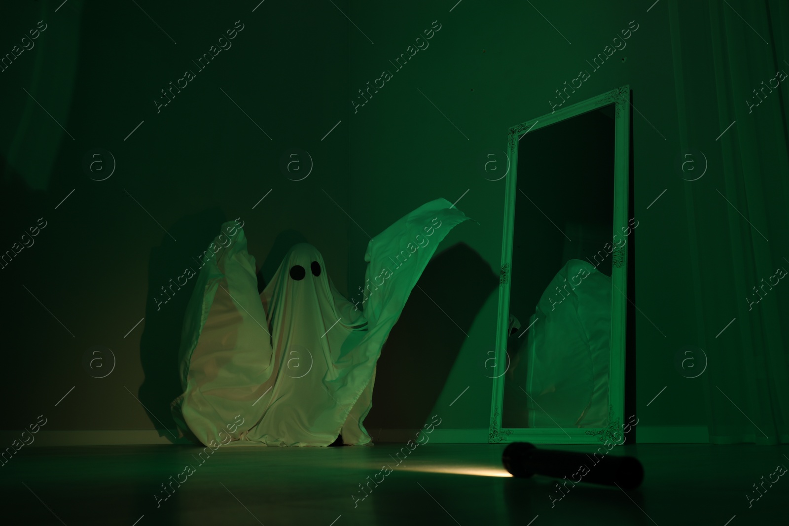 Photo of Creepy ghost. Woman covered with sheet near mirror in green light