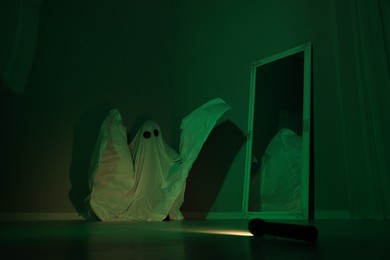 Creepy ghost. Woman covered with sheet near mirror in green light