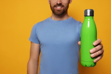 Man with green thermo bottle against orange background, closeup. Space for text