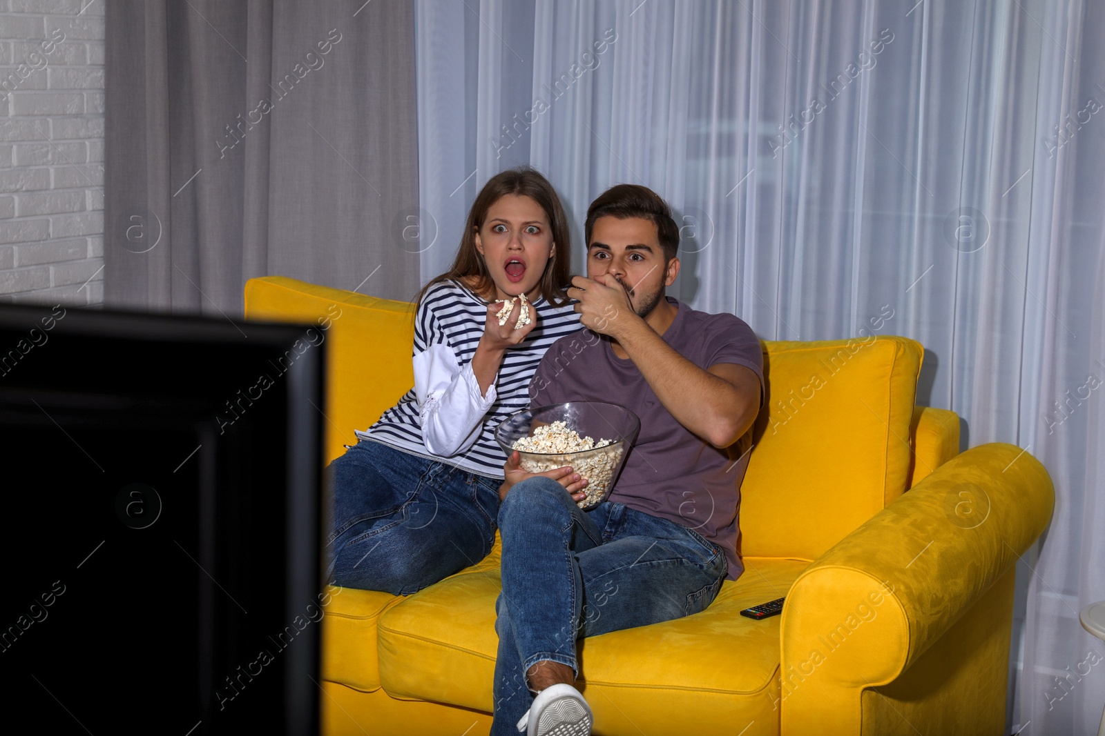 Photo of Couple with popcorn watching TV together on sofa in living room