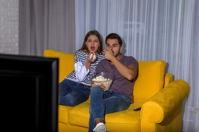 Couple with popcorn watching TV together on sofa in living room