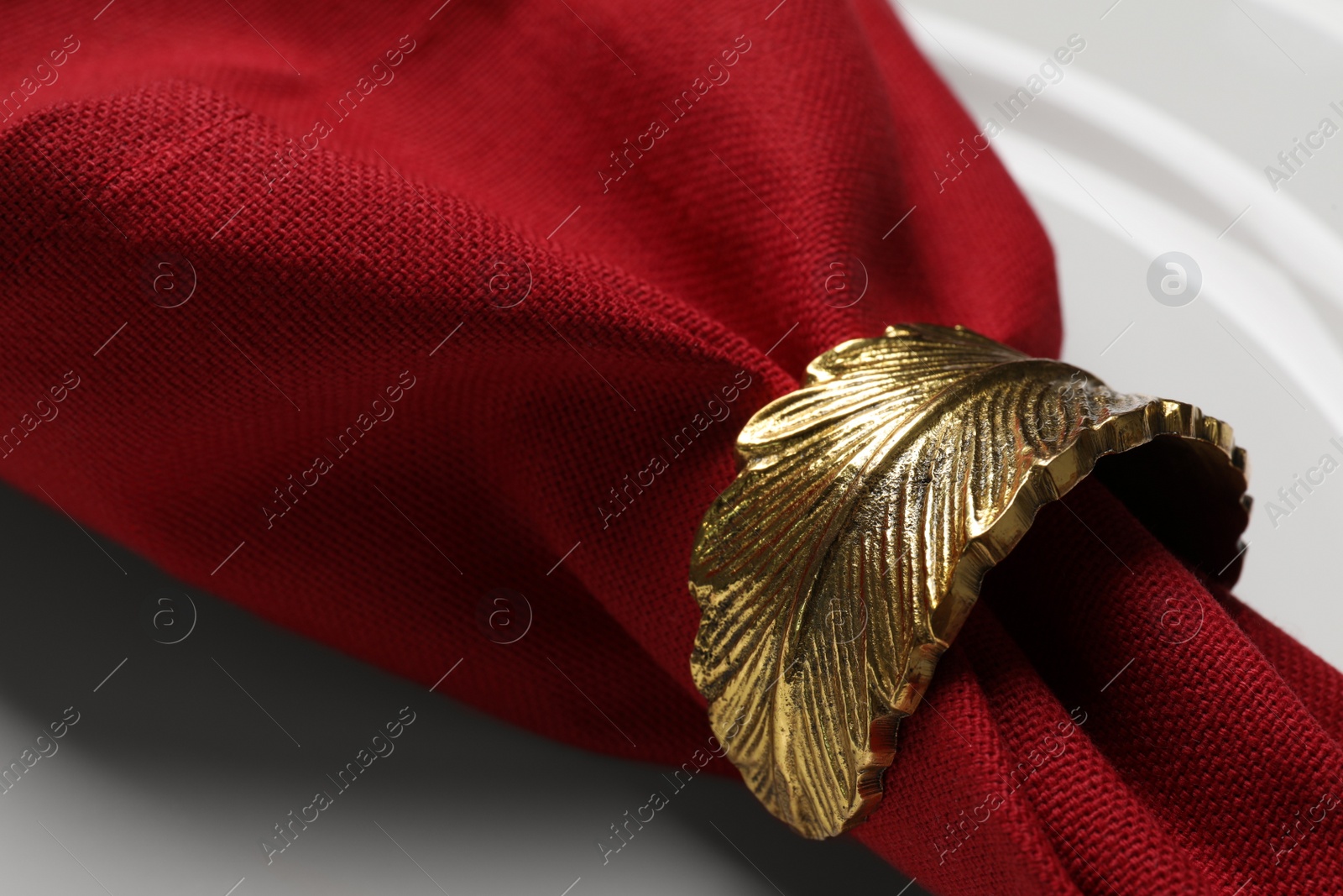 Photo of Red fabric napkin and decorative ring for table setting on white plate, closeup