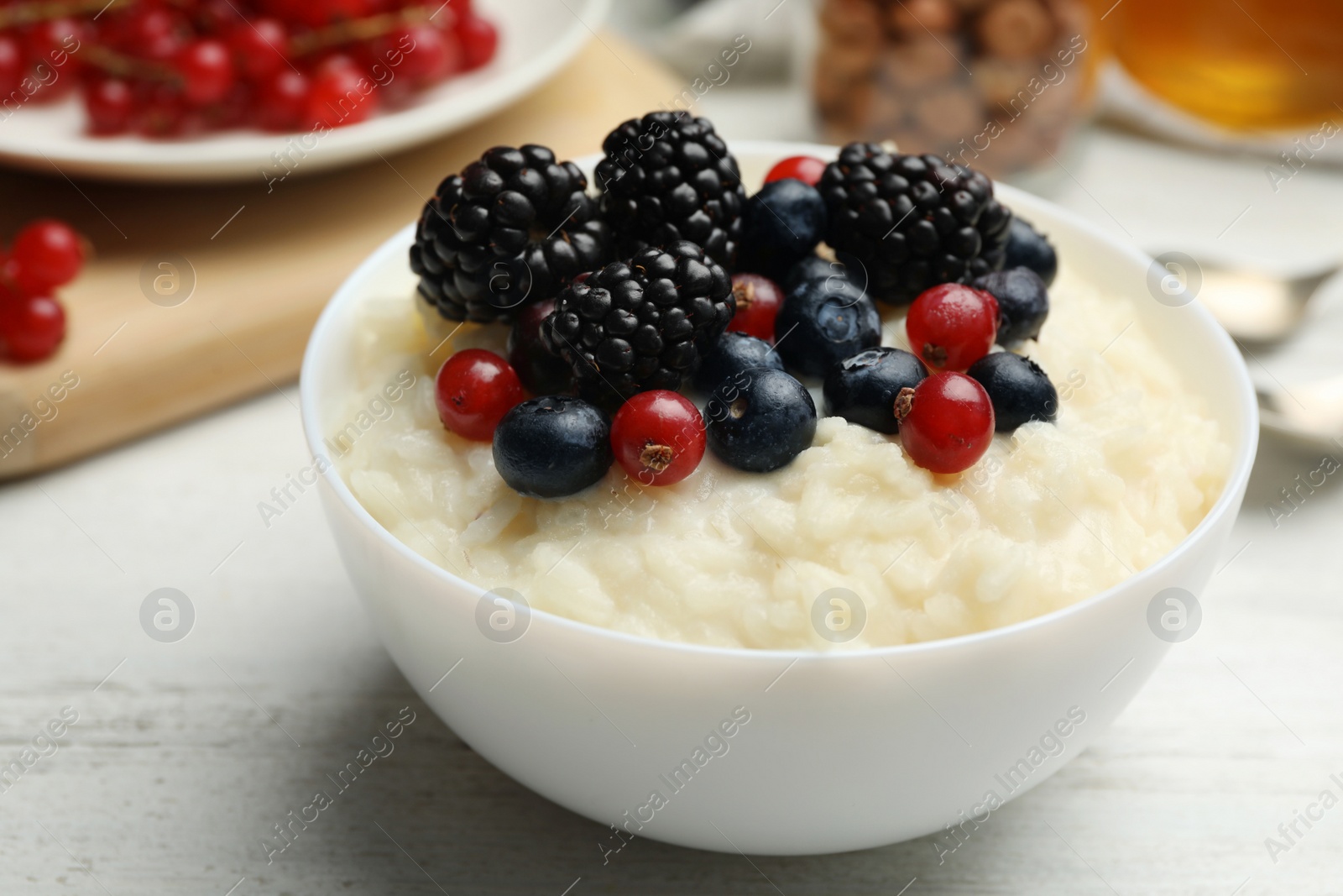 Photo of Delicious rice pudding with berries on white wooden table, closeup