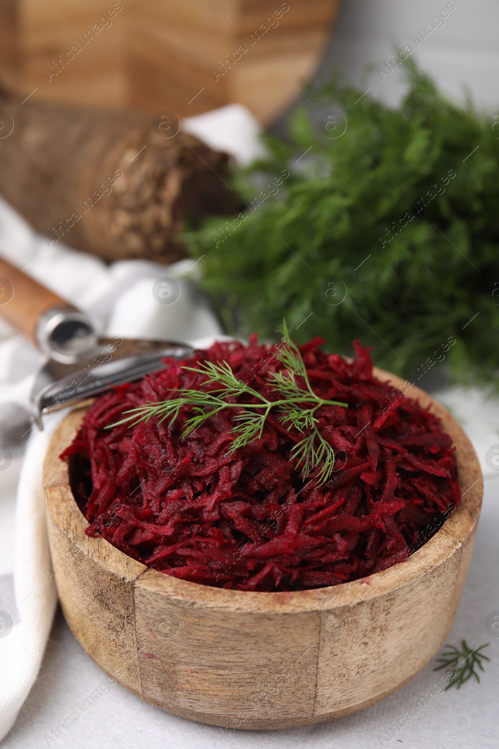 Photo of Grated red beet and dill in wooden bowl on table, closeup
