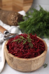 Grated red beet and dill in wooden bowl on table, closeup