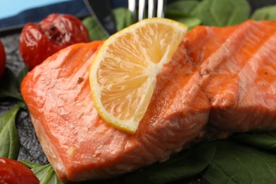 Photo of Tasty grilled salmon with tomatoes, spinach and lemon on plate, closeup