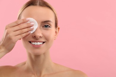 Smiling woman removing makeup with cotton pad on pink background, closeup. Space for text
