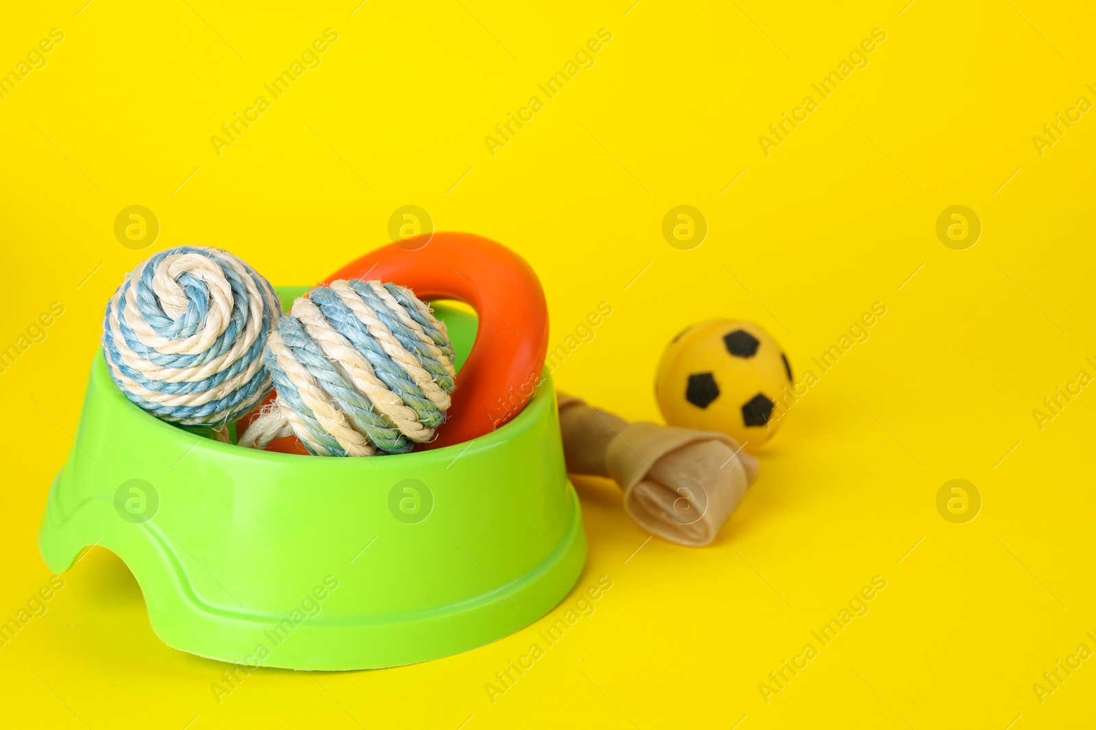 Photo of Various bright pet toys and bowl on yellow background, space for text