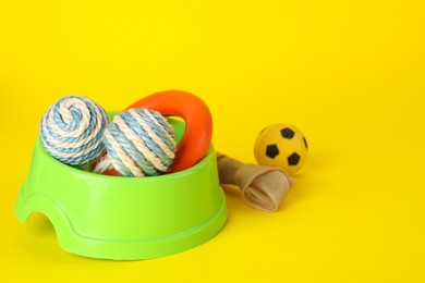Photo of Various bright pet toys and bowl on yellow background, space for text