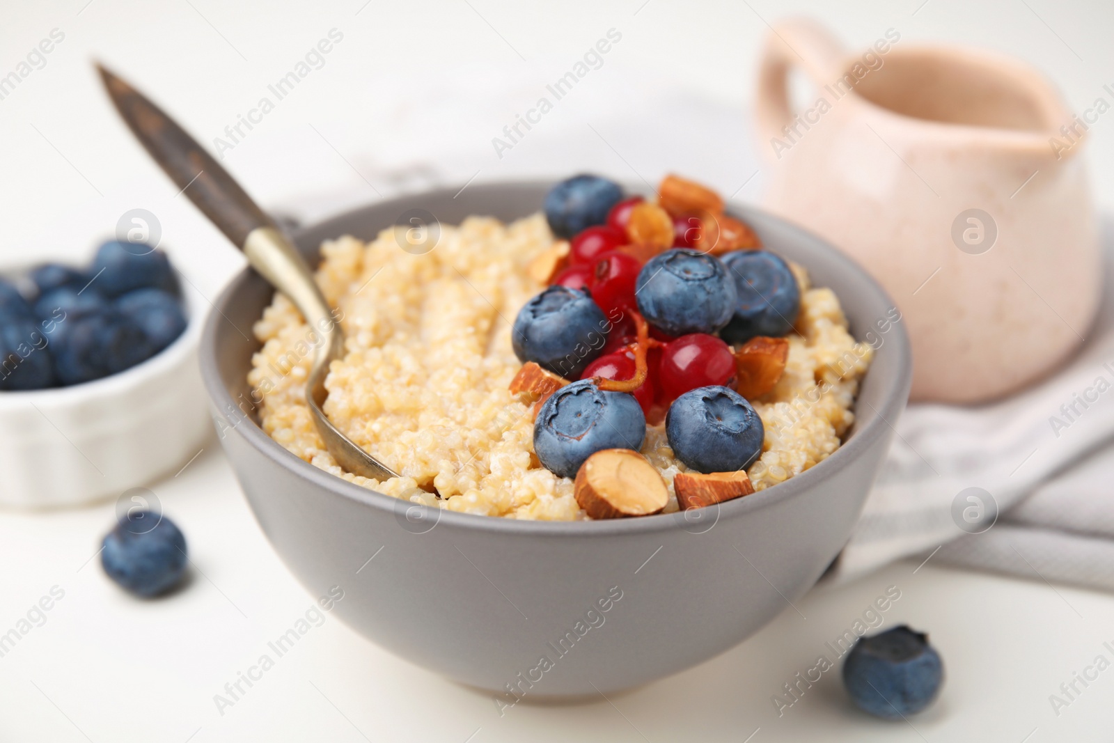 Photo of Bowl of delicious cooked quinoa with almonds, cranberries and blueberries on white table, closeup