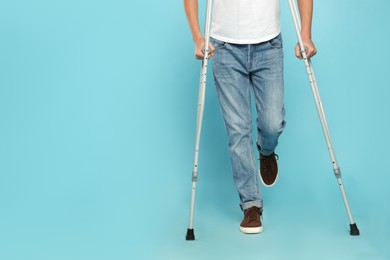 Photo of Man with injured leg using crutches on turquoise background, closeup. Space for text