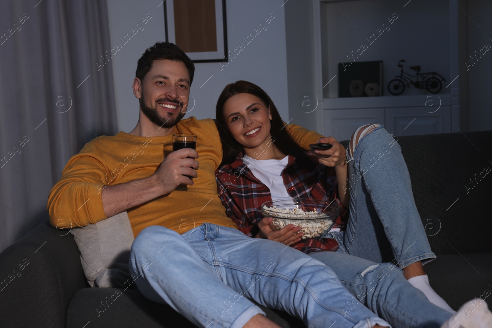 Photo of Happy couple with popcorn watching TV at home in evening