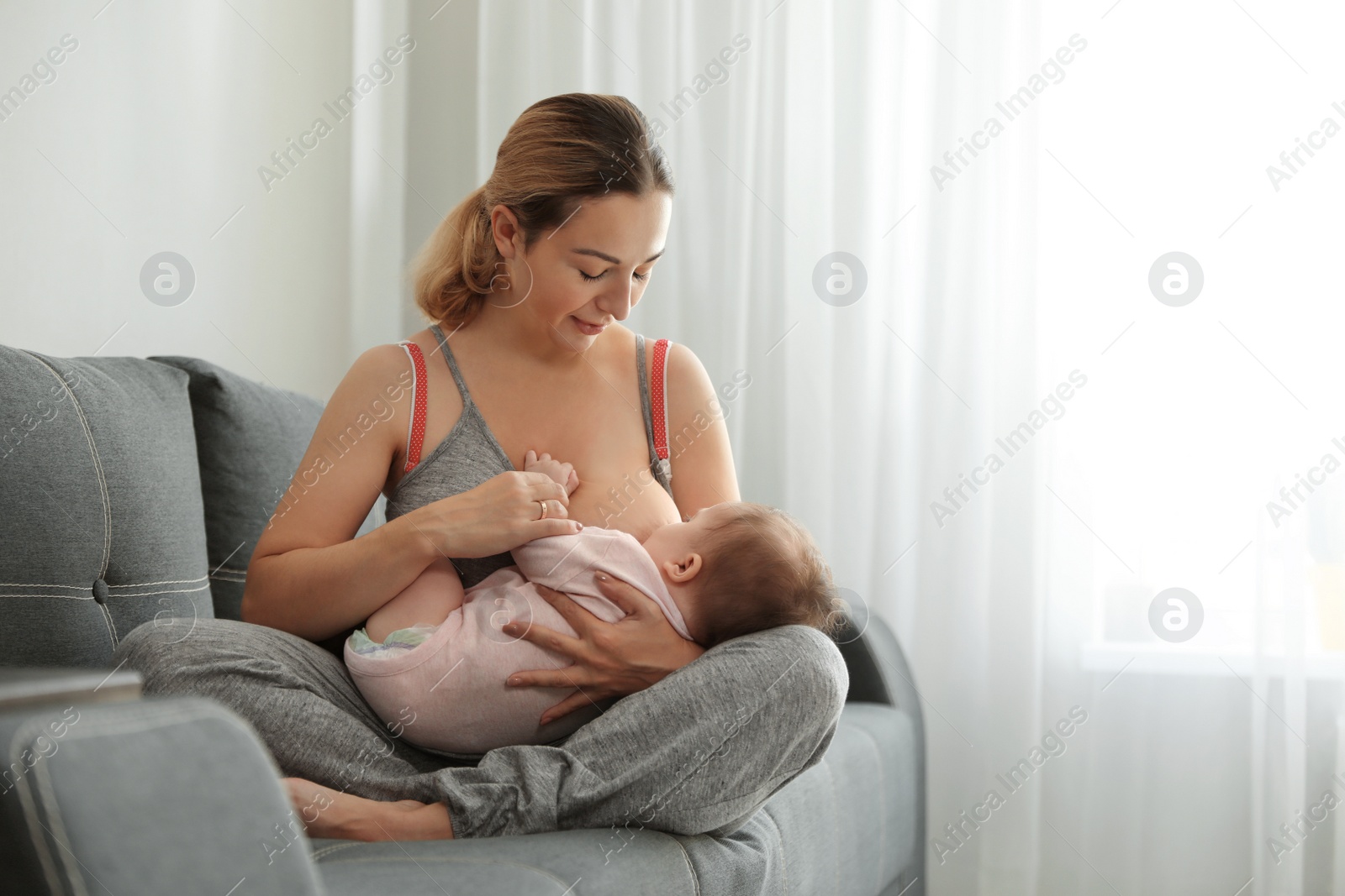 Photo of Young woman breastfeeding her baby at home. Space for text