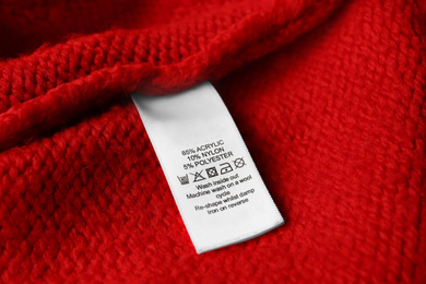 Photo of Clothing label with care symbols and material content on red sweater, closeup view