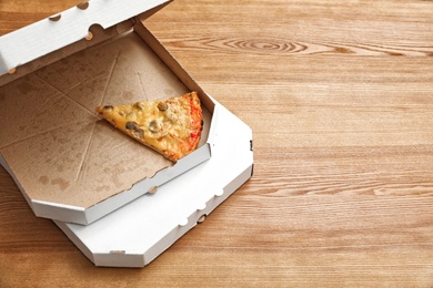 Cardboard boxes and pizza piece on wooden table. Space for text