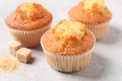 Delicious sweet muffins and brown sugar on light grey textured table, closeup