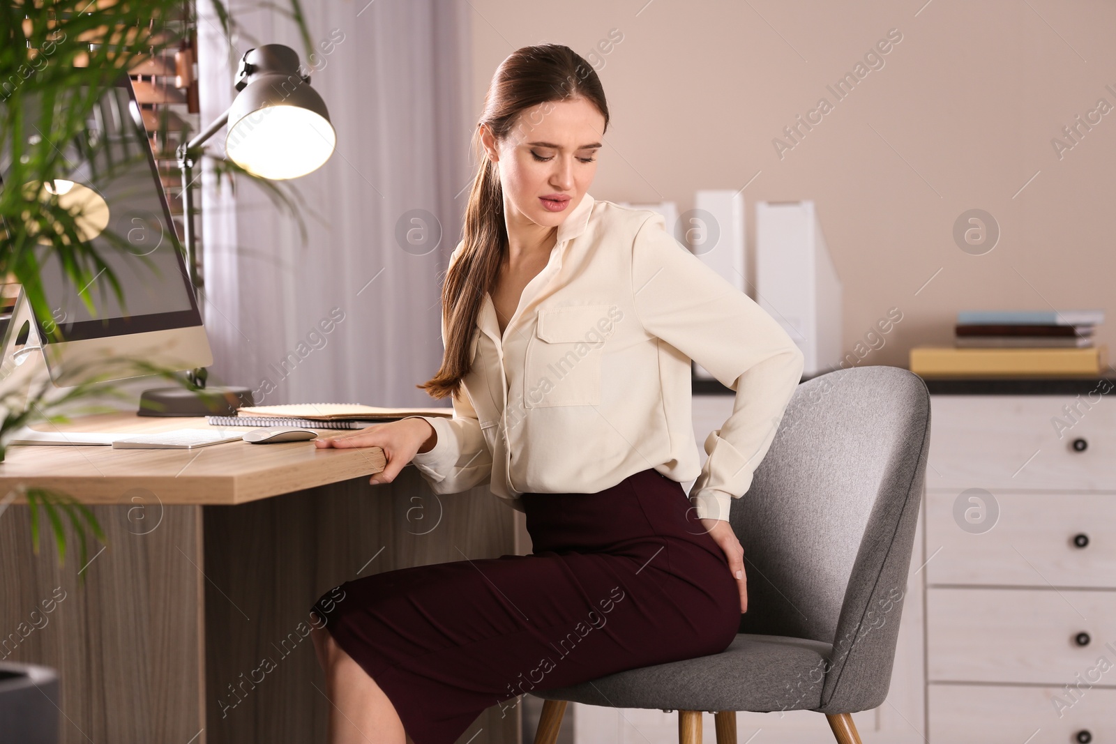 Photo of Young woman suffering from hemorrhoid at workplace in office