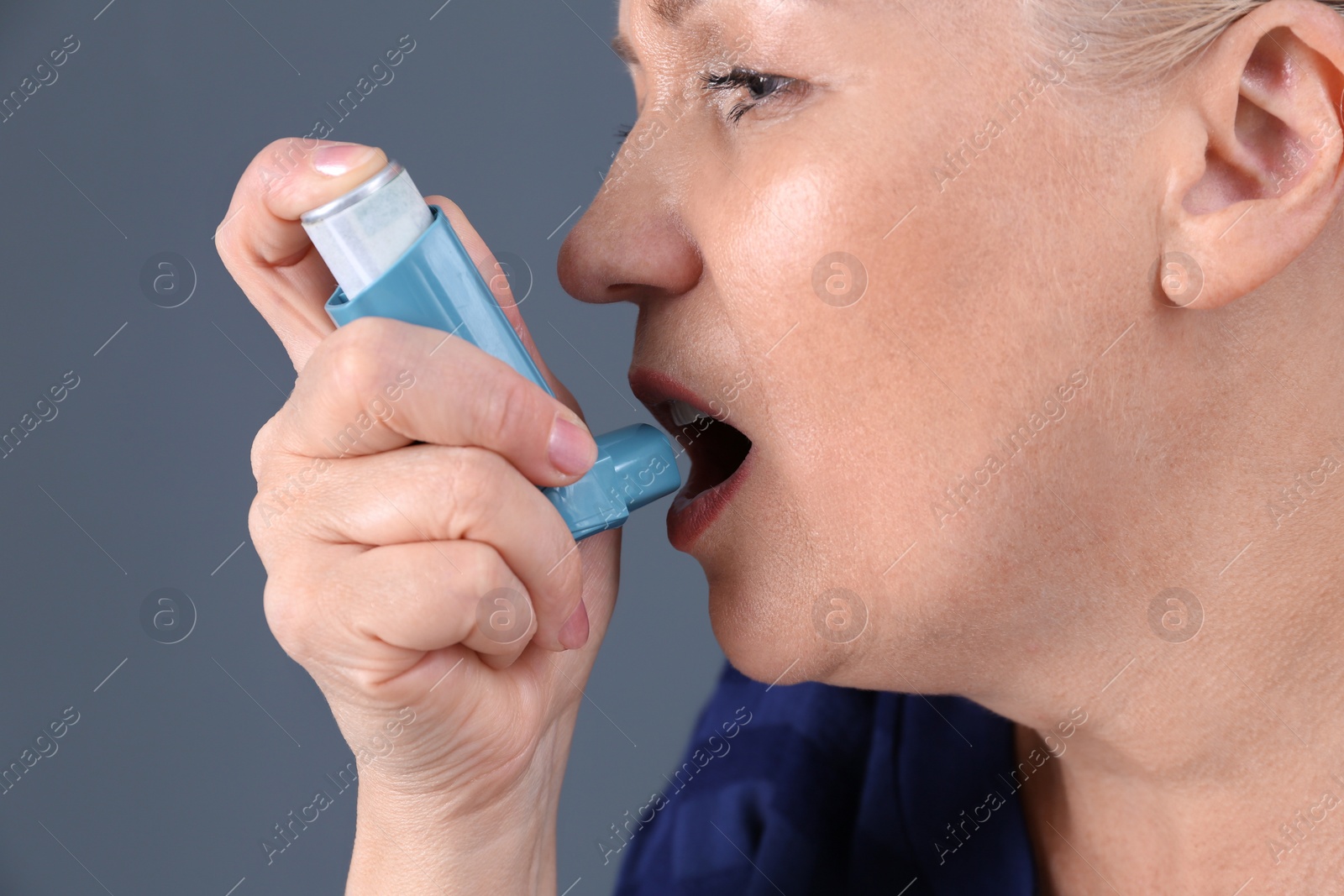 Photo of Woman using asthma inhaler on color background, closeup