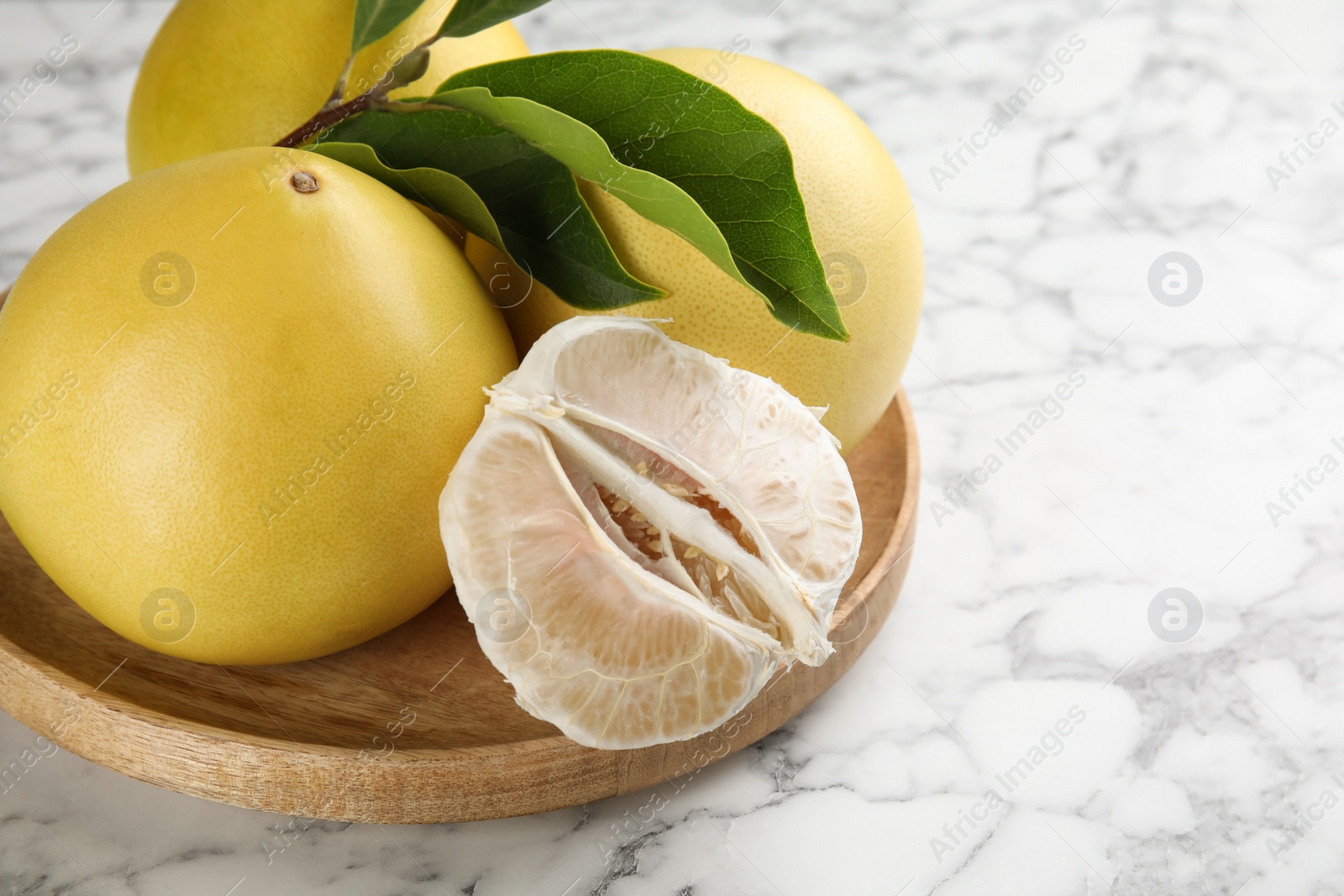 Photo of Fresh cut and whole pomelo fruits with leaves on white marble table, closeup. Space for text