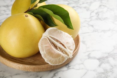 Photo of Fresh cut and whole pomelo fruits with leaves on white marble table, closeup. Space for text