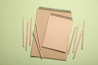 Photo of Stylish kraft notebooks and coloured pencils on light green background, flat lay