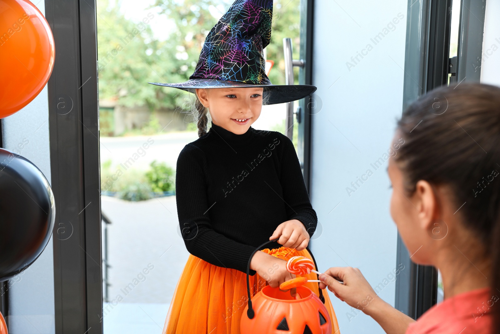 Photo of Cute little girl dressed as witch trick-or-treating at doorway. Halloween tradition