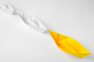 Photo of Paper boats following yellow one on white background, above view. Leadership concept