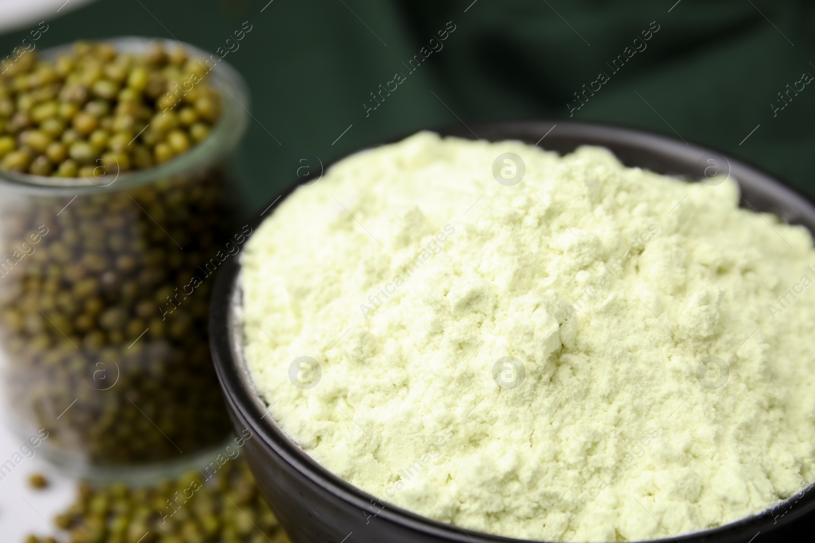 Photo of Mung bean flour in bowl and seeds on table, closeup