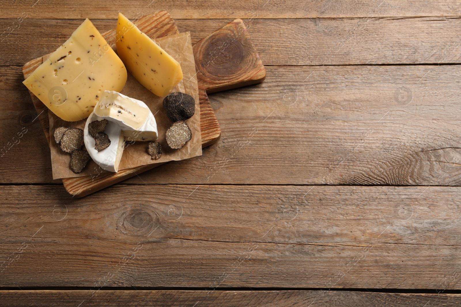 Photo of Board with delicious cheeses and fresh black truffles on wooden table, top view. Space for text