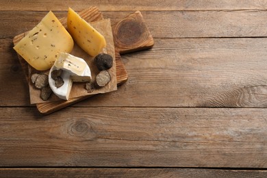 Photo of Board with delicious cheeses and fresh black truffles on wooden table, top view. Space for text