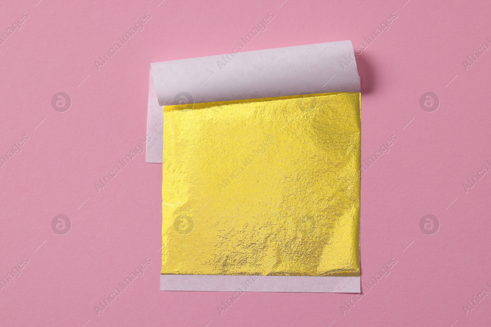 Photo of Edible gold leaf sheet on pink background, top view
