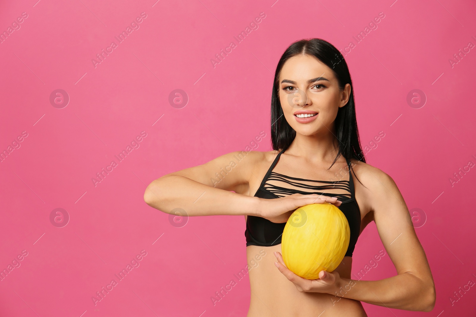 Photo of Beautiful young woman in black bikini with melon on pink background. Space for text