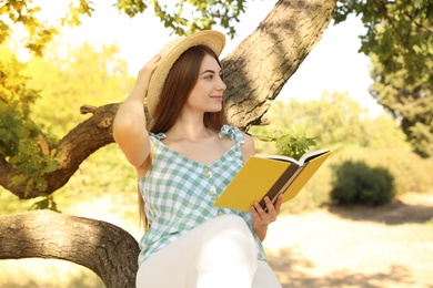 Photo of Young woman reading book on tree in park