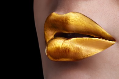 Image of Young woman with beautiful gold lips on black background, closeup