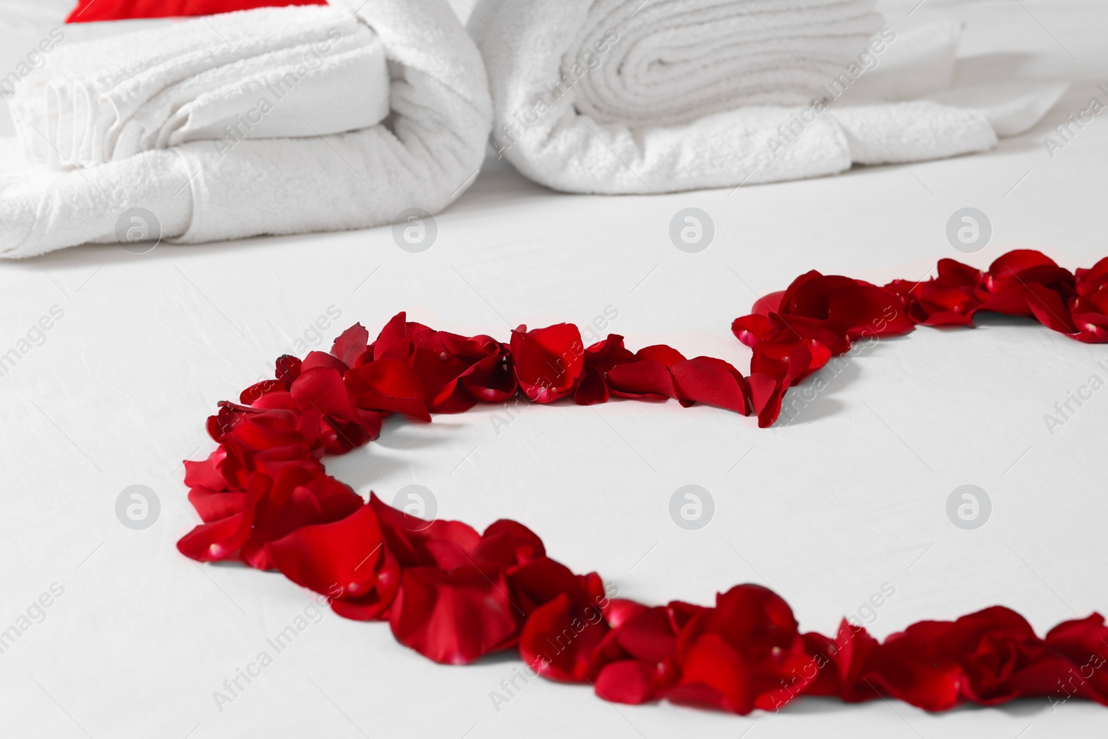 Photo of Honeymoon. Heart made with rose petals on bed, closeup