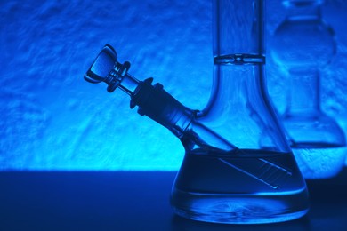 Photo of Closeup view of glass bongs on table, toned in blue. Smoking device