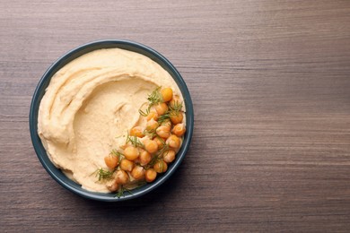 Photo of Bowl of tasty hummus with chickpeas and dill on wooden table, top view. Space for text