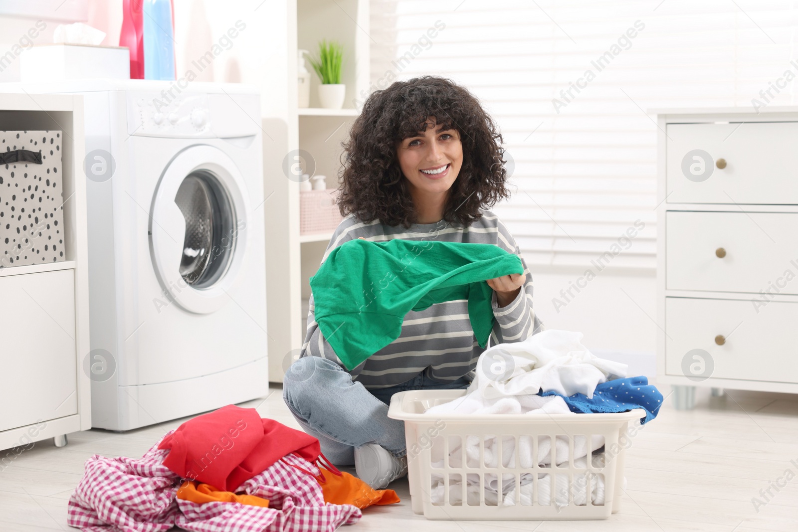 Photo of Happy woman with laundry near washing machine indoors