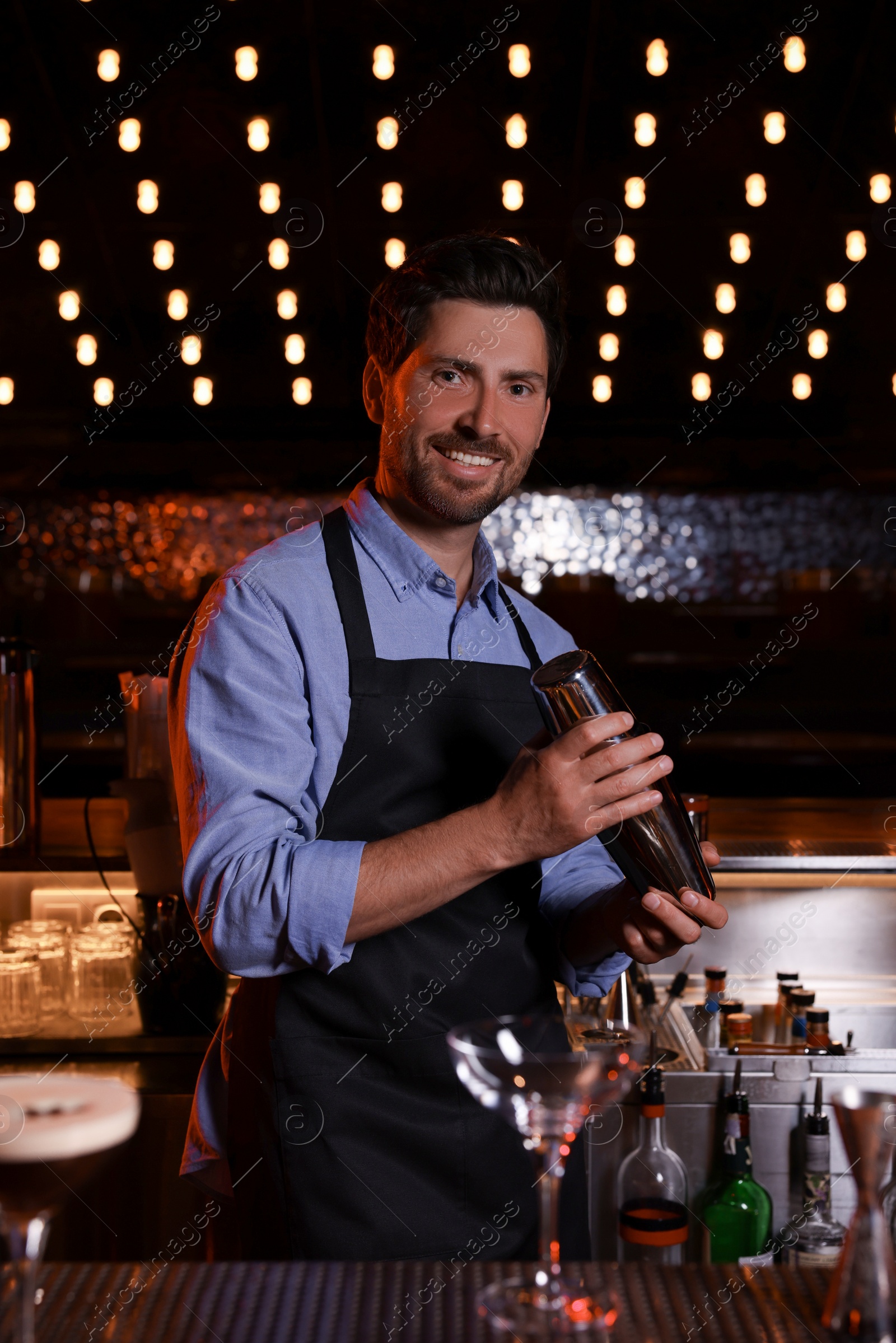 Photo of Bartender with shaker preparing fresh alcoholic cocktail in bar