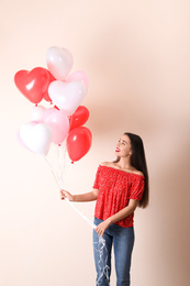 Photo of Beautiful young woman with heart shaped balloons on beige background. Valentine's day celebration