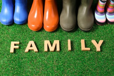 Photo of Rainboots and word Family made of wooden letters on green grass, above view