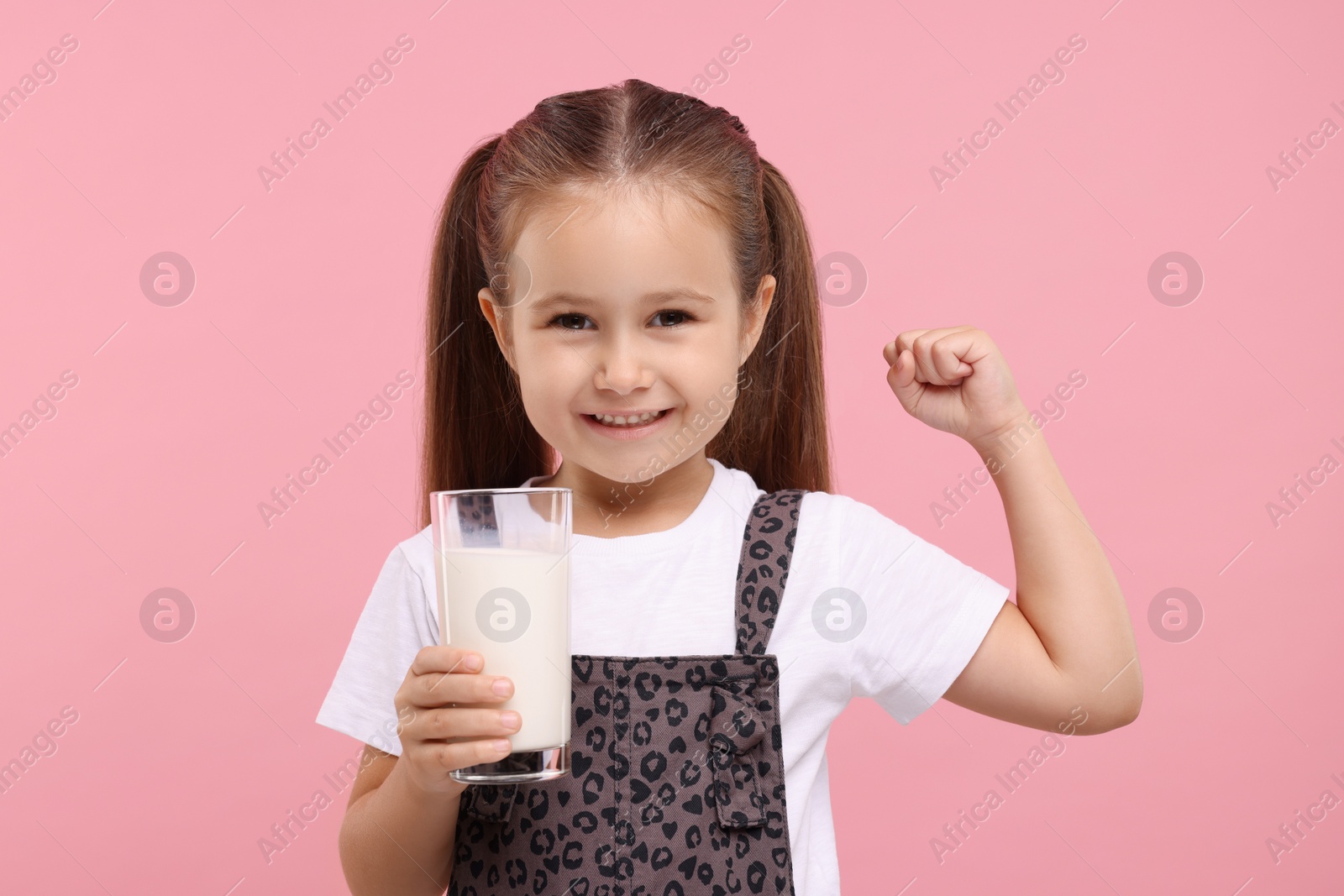 Photo of Cute girl with glass of fresh milk showing her strength on pink background
